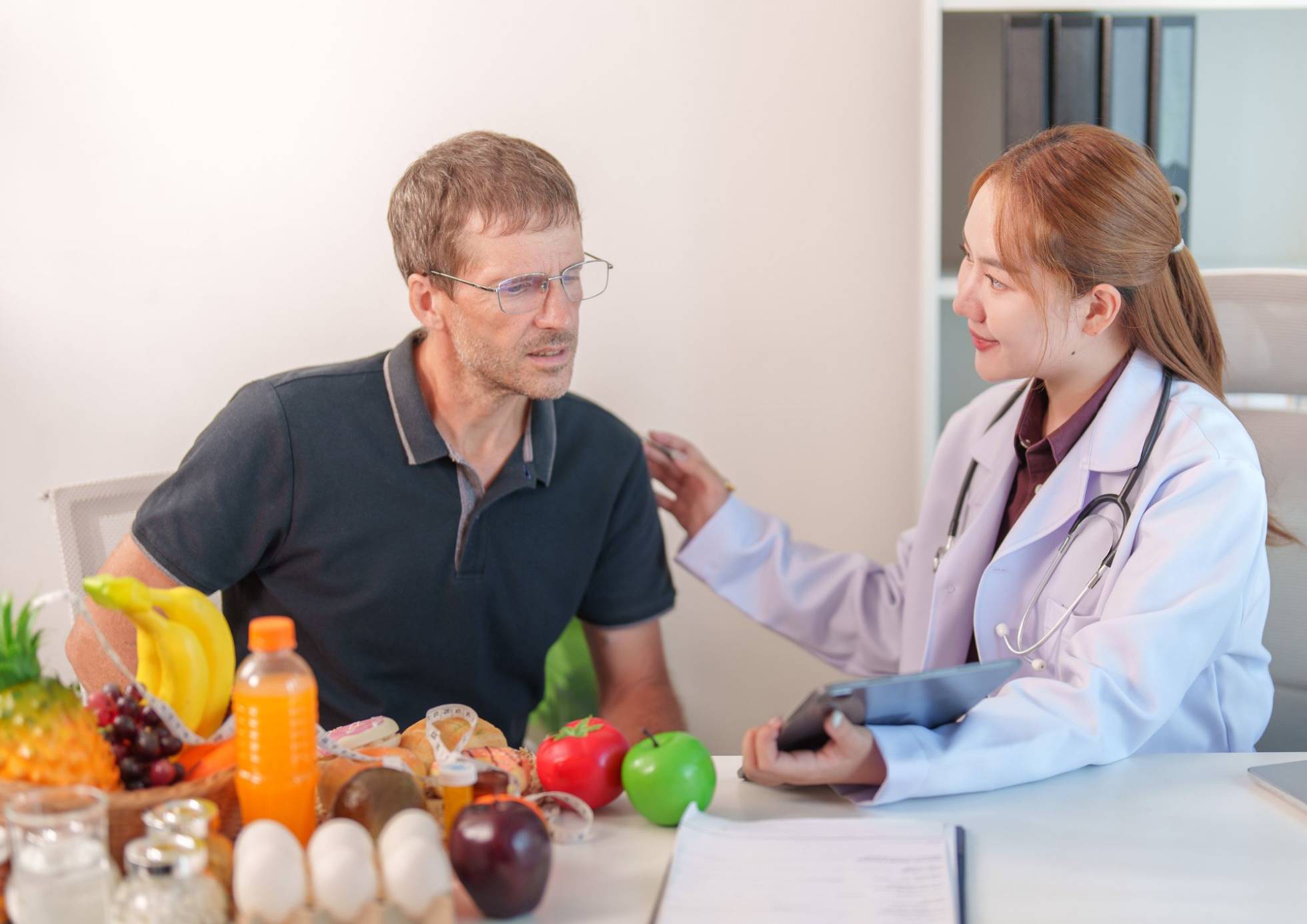 What Is A Nutrition Coach? 3 A doctor discusses health with a man and woman at a table filled with fresh fruits and vegetables.