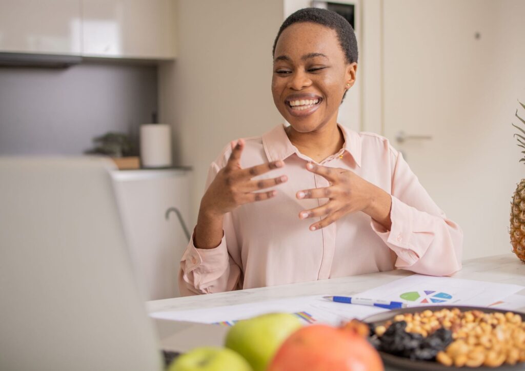 What Is A Nutrition Coach? 4 A woman smiles at a table adorned with fruit and a laptop, suggesting a relaxed and productive atmosphere.