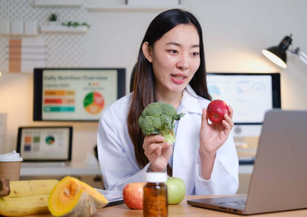 What Is A Nutrition Coach? 5 A woman in a lab coat holds a piece of fruit and a vegetable, symbolising health and nutrition in a laboratory setting.