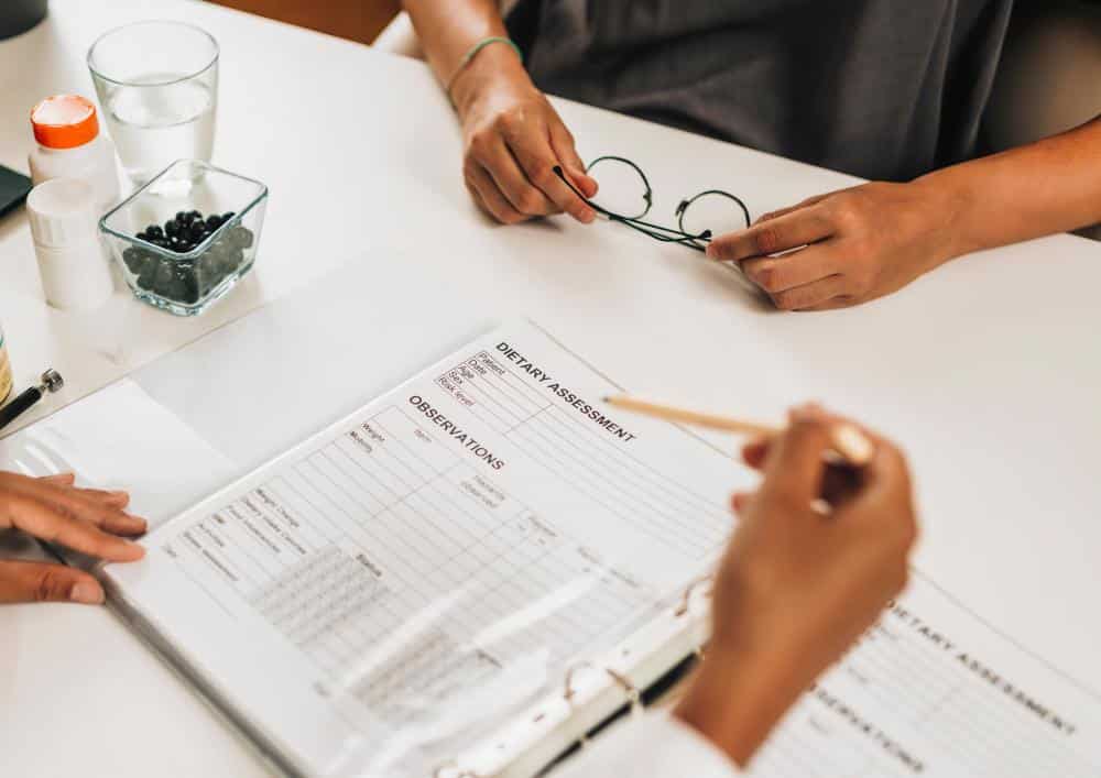 What Is A Clinical Nutritionist? 5 A woman seated at a table holds a clipboard and pen, appearing focused on her notes or tasks.