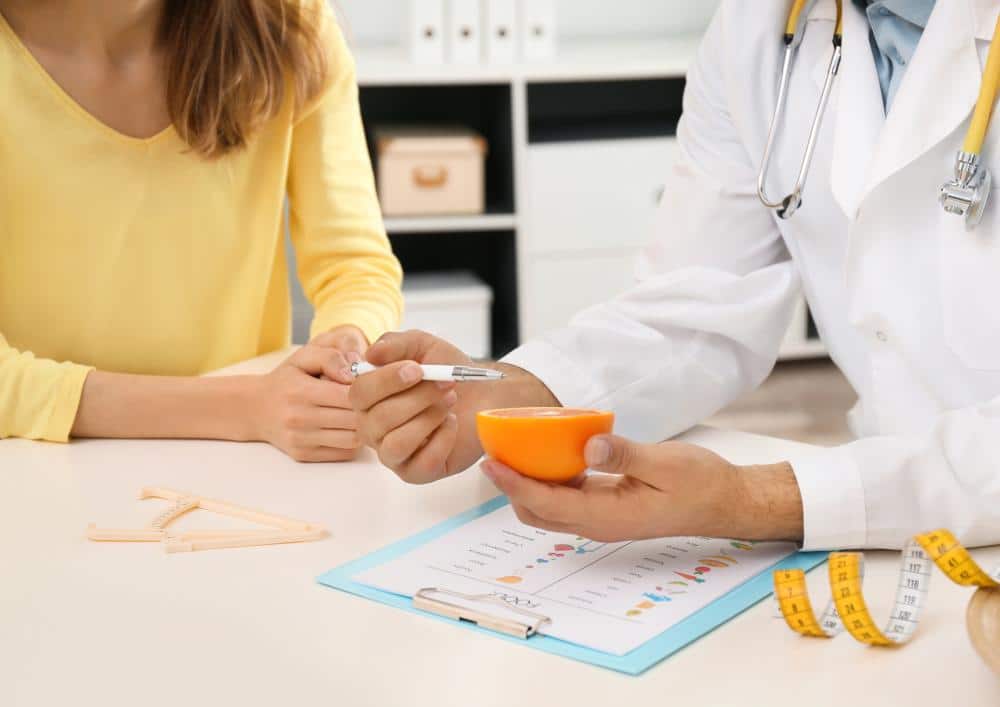What Is A Clinical Nutritionist? 6 A doctor presents an orange to a woman, symbolising health and nutrition during a consultation.
