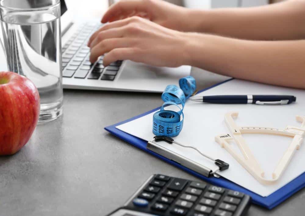 What Is A Clinical Nutritionist? 7 A person typing on a laptop, with an apple and a calculator placed on the table beside them.