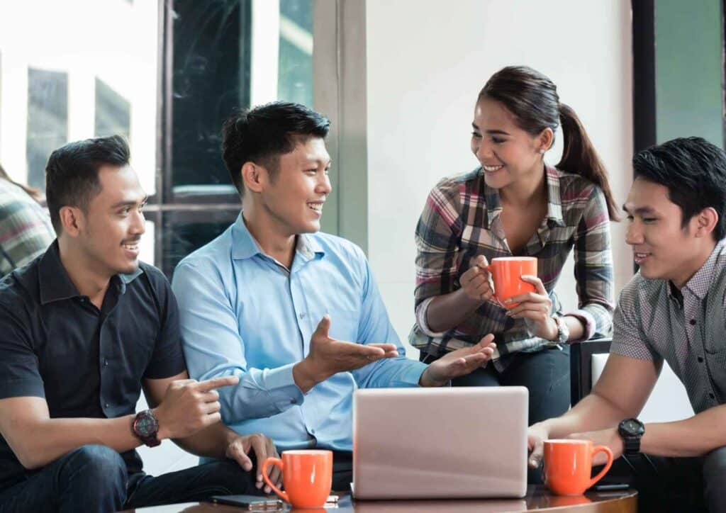What Is Corporate Nutrition? 5 Asian business professionals engaged in a discussion at a coffee shop, surrounded by a warm and inviting atmosphere.