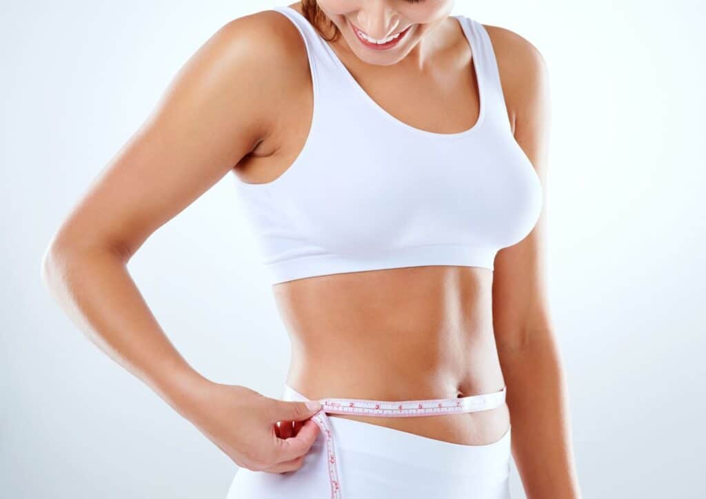 What Is A Weight Loss Nutritionist? 8 A woman in a white sports bra measures her waist with a tape measure, focusing on her fitness routine.