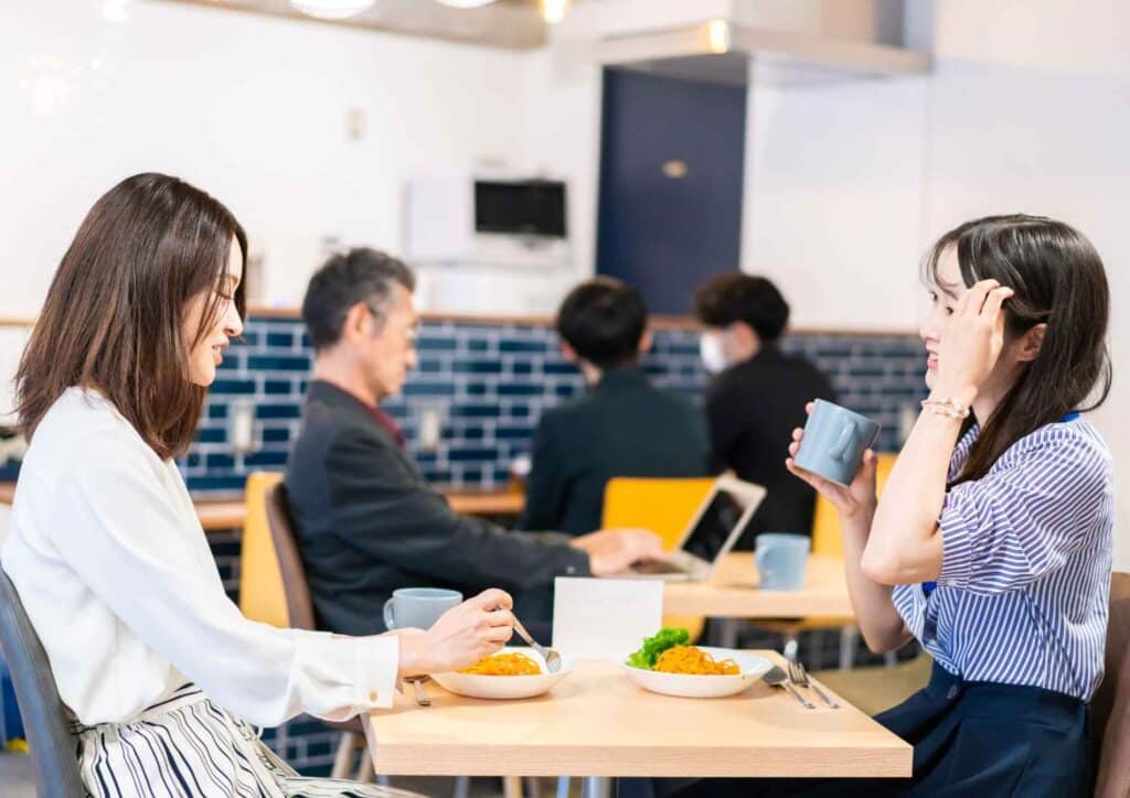 What Is Corporate Nutrition? 2 Two women engaged in conversation while sitting at a table in a restaurant, enjoying their meal together.