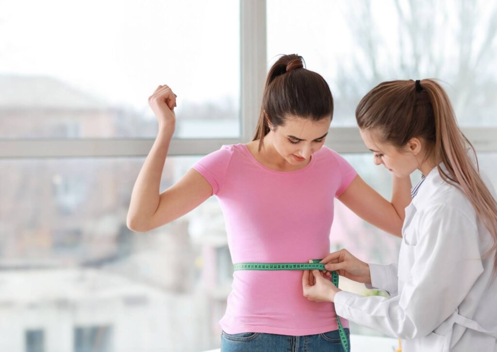 What Is A Weight Loss Nutritionist? 1 A woman measures her waist with a doctor, who observes and provides guidance during a health assessment.