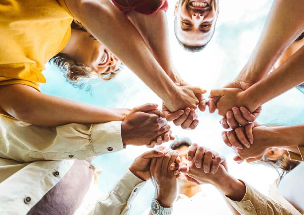 What Is School Wellbeing? 4 A diverse group of people standing in a circle, holding hands, symbolising unity and togetherness.
