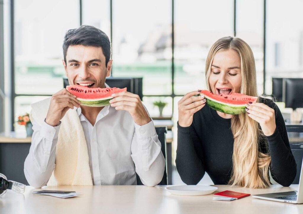 Corporate Nutrition Speaker Workplace Benefits 7 A woman eats lettuce while two men observe her, engaged in conversation.