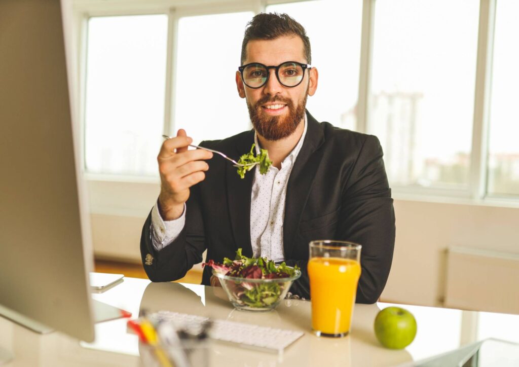 Corporate Nutrition Speaker Workplace Benefits 4 A man in a suit enjoys a salad while sipping juice, seated at a table in a casual dining setting.
