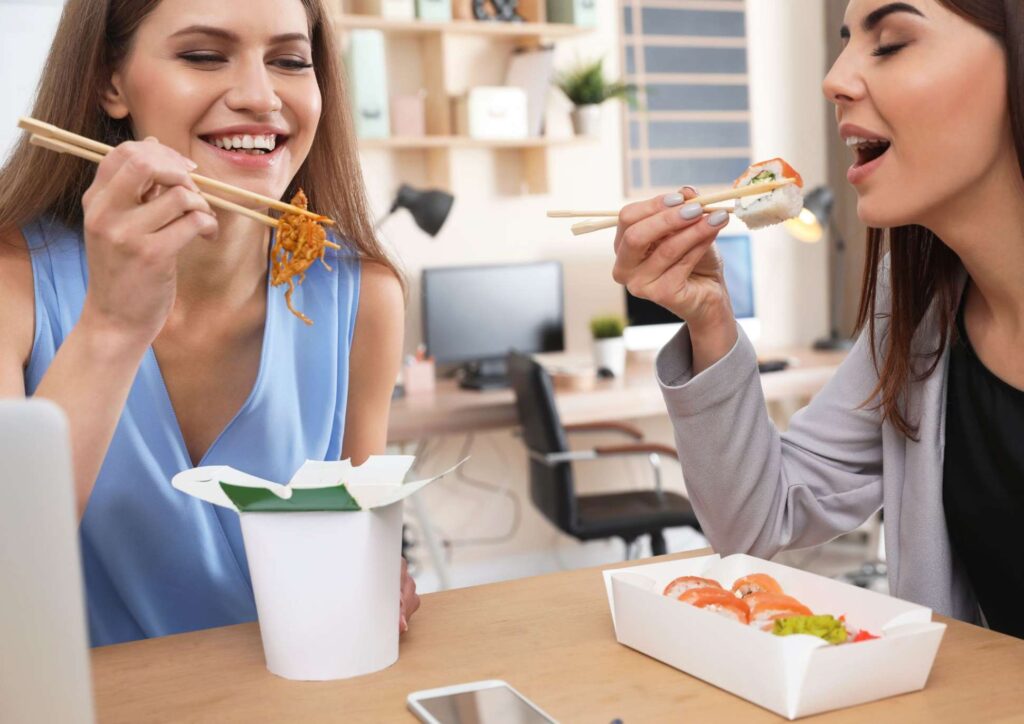 Corporate Nutrition Speaker Workplace Benefits 2 Two women enjoying sushi together, each holding chopsticks, smiling and engaged in conversation.