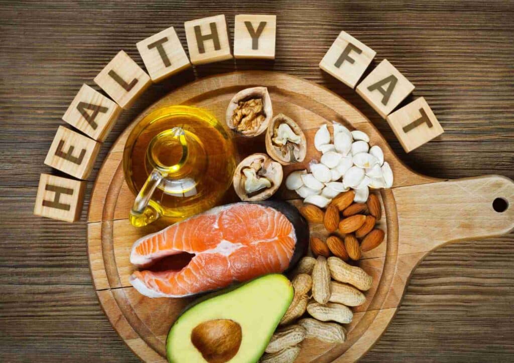 Nutrition For Runners 5 A variety of healthy fat foods including avocados, nuts, and olive oil displayed on a wooden table.