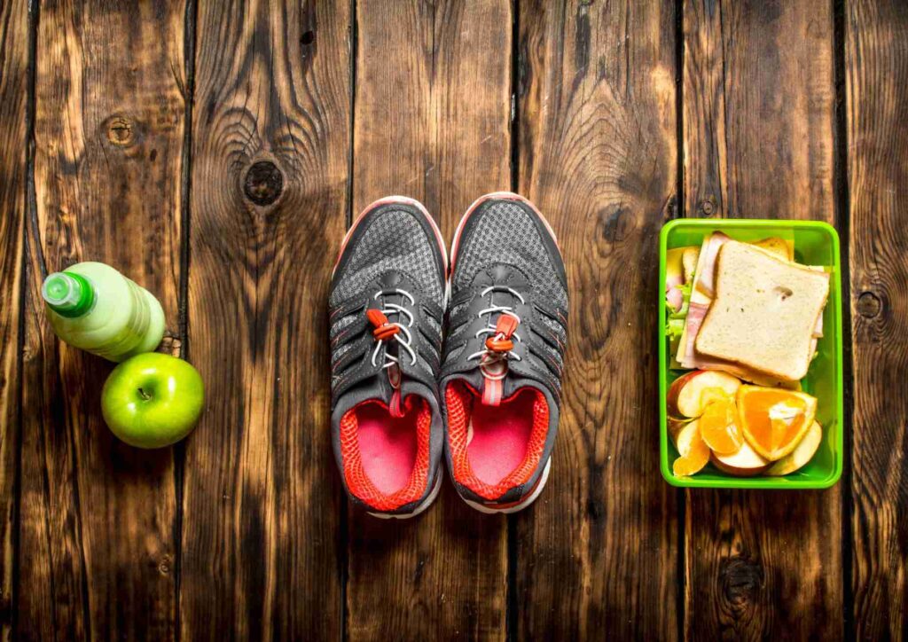 Nutrition For Runners 1 A pair of running shoes, a sandwich, an apple, and a water bottle arranged on a wooden table.