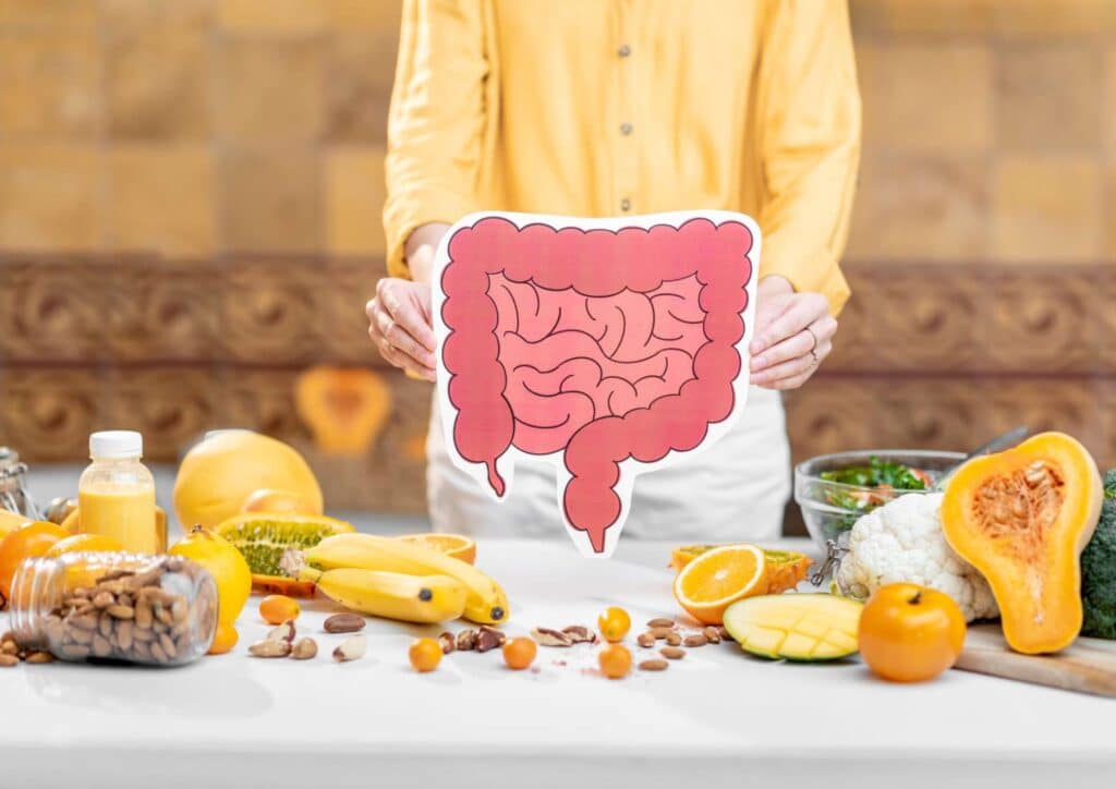 What Is The Perfect Diet? 6 A woman holds a cutout of a human stomach, surrounded by various fruits and vegetables on a table.