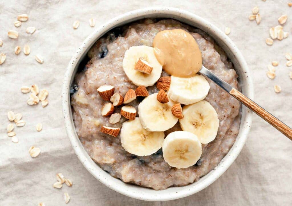 Nutrition For Runners 8 A bowl of oatmeal topped with sliced banana, almonds, and a dollop of peanut butter.