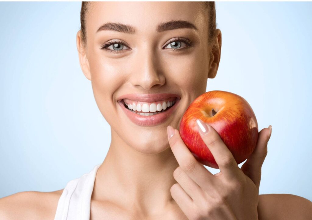 What Is The Perfect Diet? 7 A woman smiling while holding a red apple in her hand, showcasing a cheerful expression.