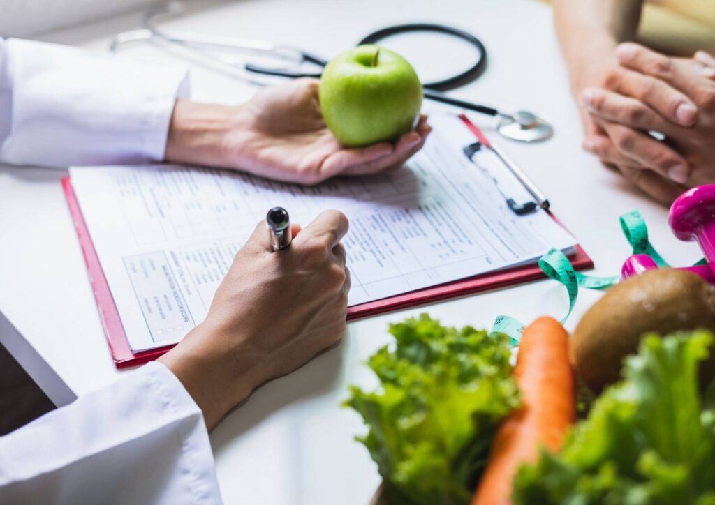 What Does a Nutritionist Do? 5 A doctor writes on a clipboard, surrounded by a green apple and fresh vegetables, emphasising healthy eating.