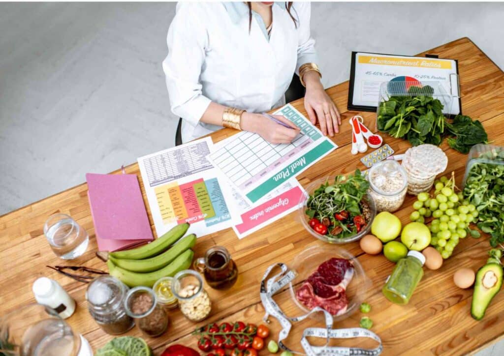 What Does a Nutritionist Do? 4 A woman writes in a notebook beside a bowl filled with fresh vegetables, indicating a focus on healthy cooking or meal planning.
