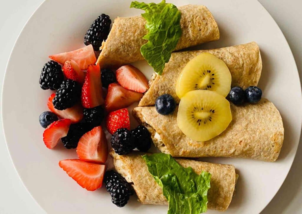 What Is The Perfect Diet? 8 A plate featuring an assortment of fresh fruit alongside a neatly wrapped sandwich.