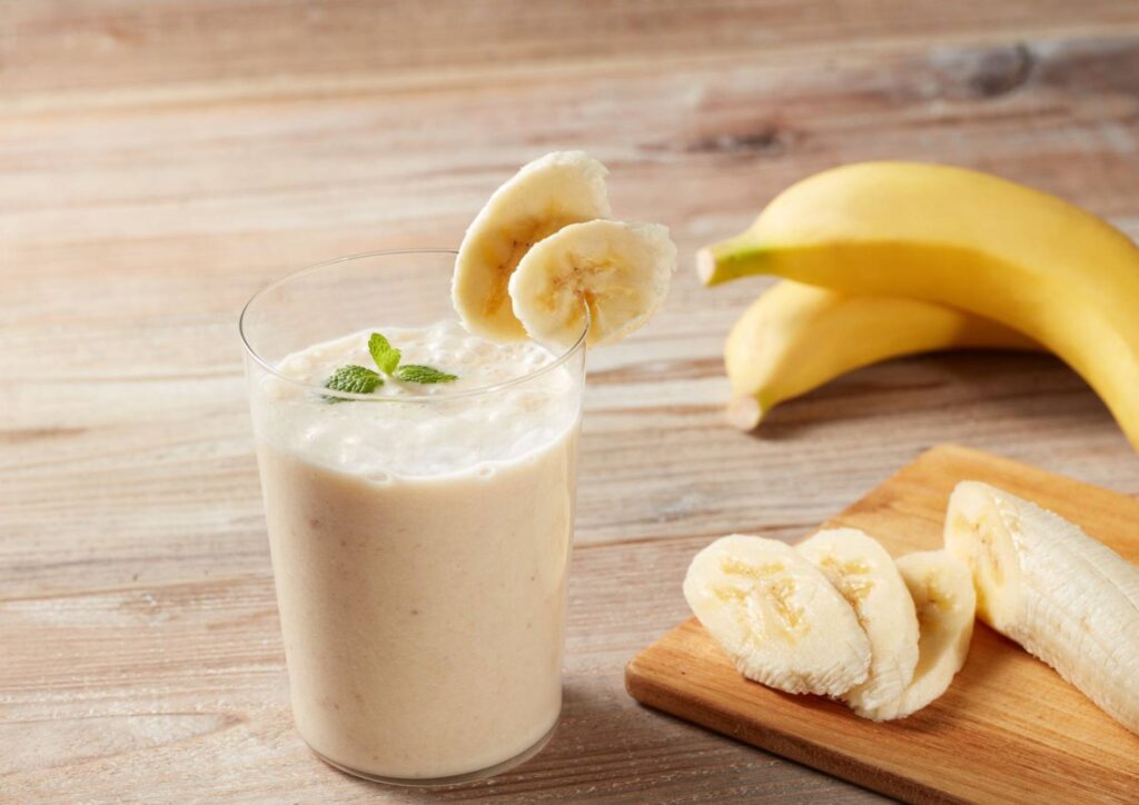 High Protein Banana Smoothie For Weight Loss 1 A ripe banana and a glass of smoothie sit on a rustic wooden table, showcasing a healthy snack option.