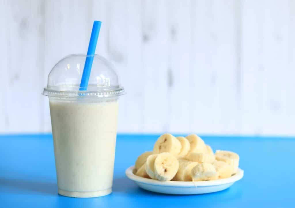 High Protein Banana Smoothie For Weight Loss 4 A banana smoothie in a glass with a blue straw, garnished with banana chips on the rim.