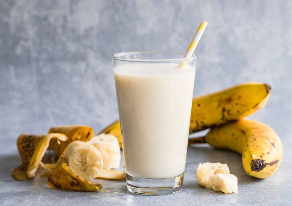High Protein Banana Smoothie For Weight Loss 2 A banana and oat smoothie in a glass, accompanied by a spoon resting on the side.