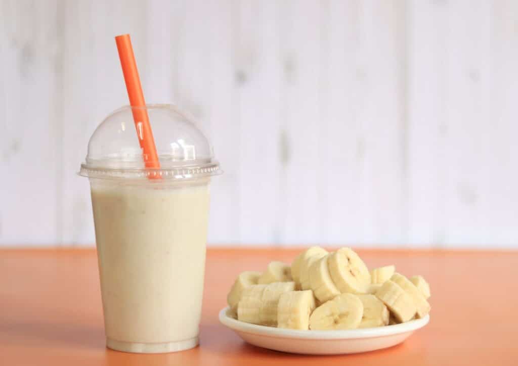 High Protein Banana Smoothie For Weight Loss 3 A smoothie in a glass, featuring bananas and a straw, placed on a wooden table.