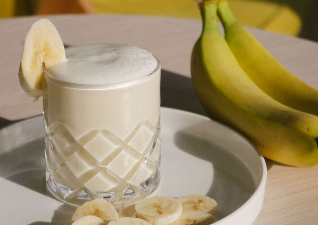 High Protein Banana Smoothie For Weight Loss 5 A ripe banana and a glass of smoothie sit on a rustic wooden table, showcasing a healthy snack option.