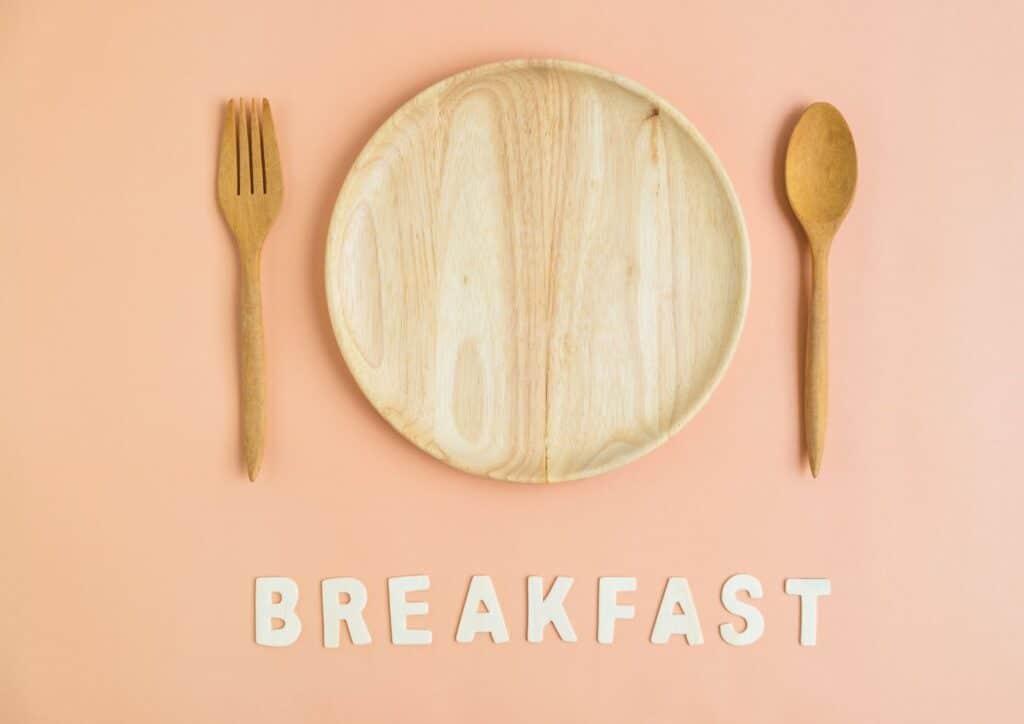 Is Breakfast the Most Important Meal of the Day? 2 A breakfast plate featuring food, accompanied by a wooden spoon and fork, set against a pink background.