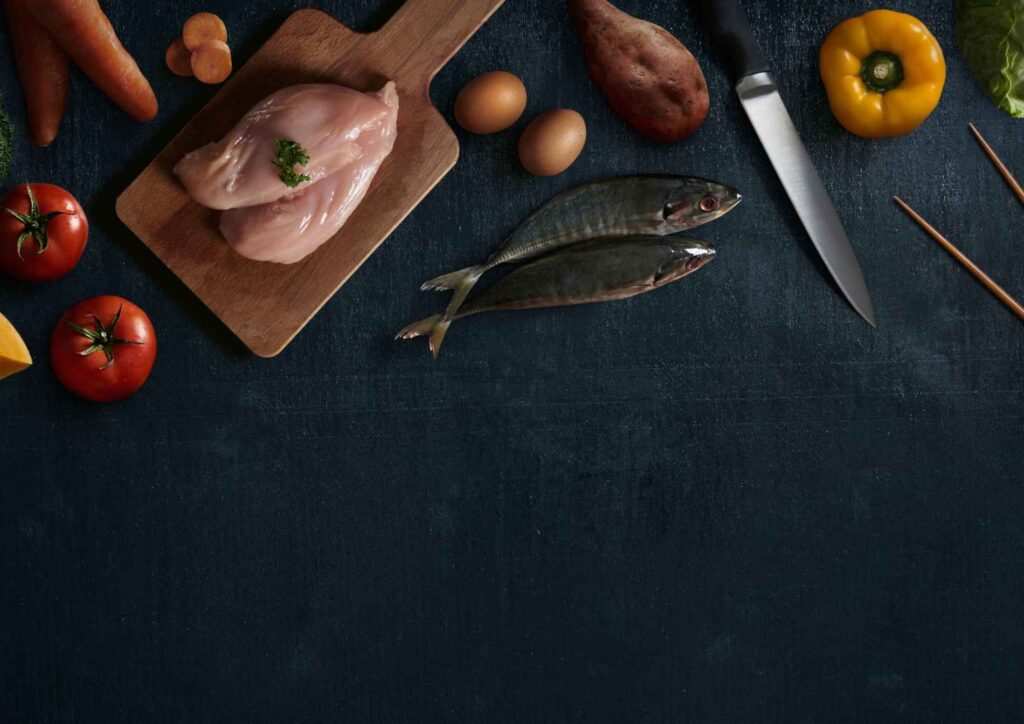 What Is A Sports Nutritionist? 1 An assortment of fresh vegetables and raw meat arranged on a wooden cutting board, ready for meal preparation.