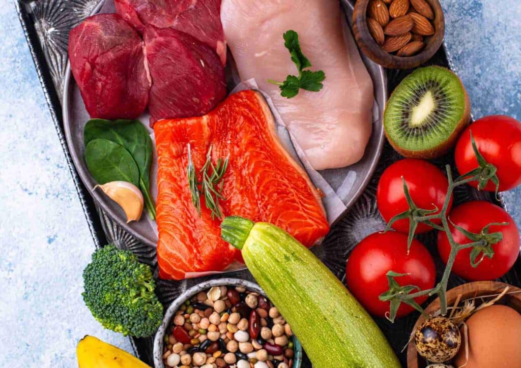 What Is A Sports Nutritionist? 8 A variety of foods including meat, fish, vegetables, and eggs arranged on a wooden surface.