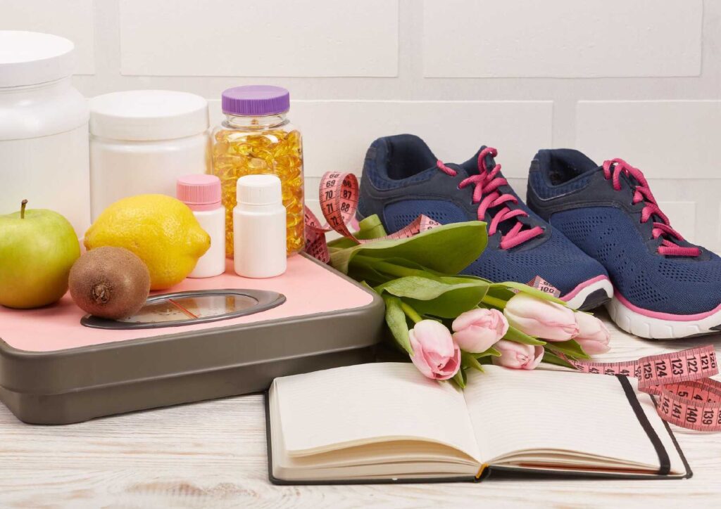 What Is A Sports Nutritionist? 6 A pink scale, sneakers, a book, a vitamin bottle, and a water bottle arranged on a flat surface.