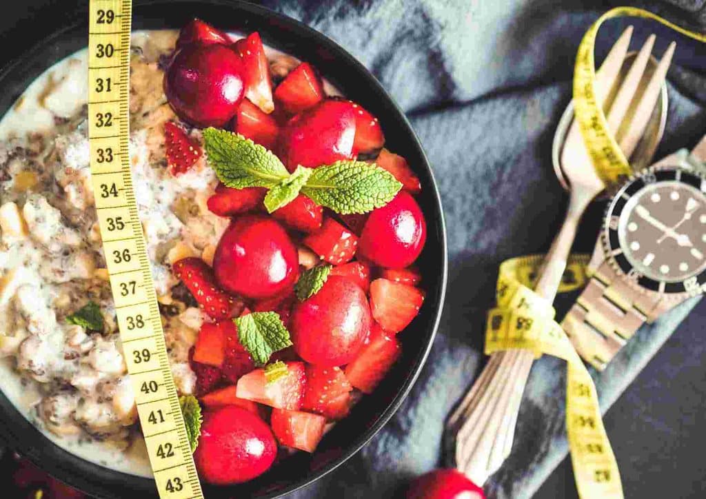 Are Oats Good for Weight Loss? 11 A bowl of oatmeal topped with fresh strawberries, accompanied by a measuring tape for portion control.