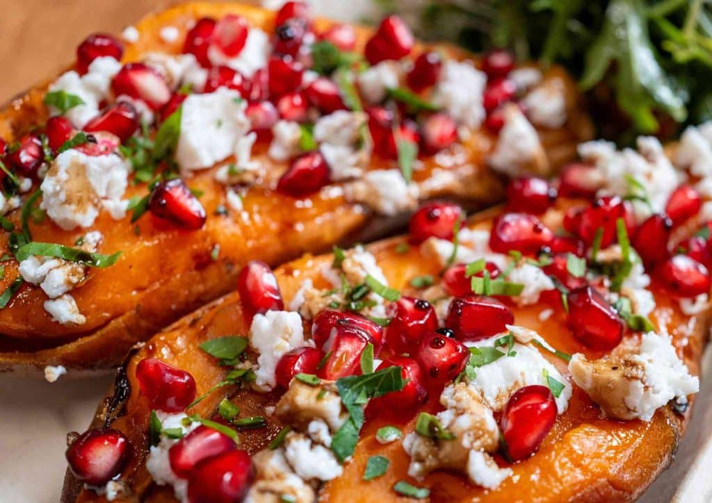 Is Sweet Potato Good for Weight Loss? 28 Grilled sweet potatoes topped with pomegranate seeds and crumbled feta cheese on a white plate.