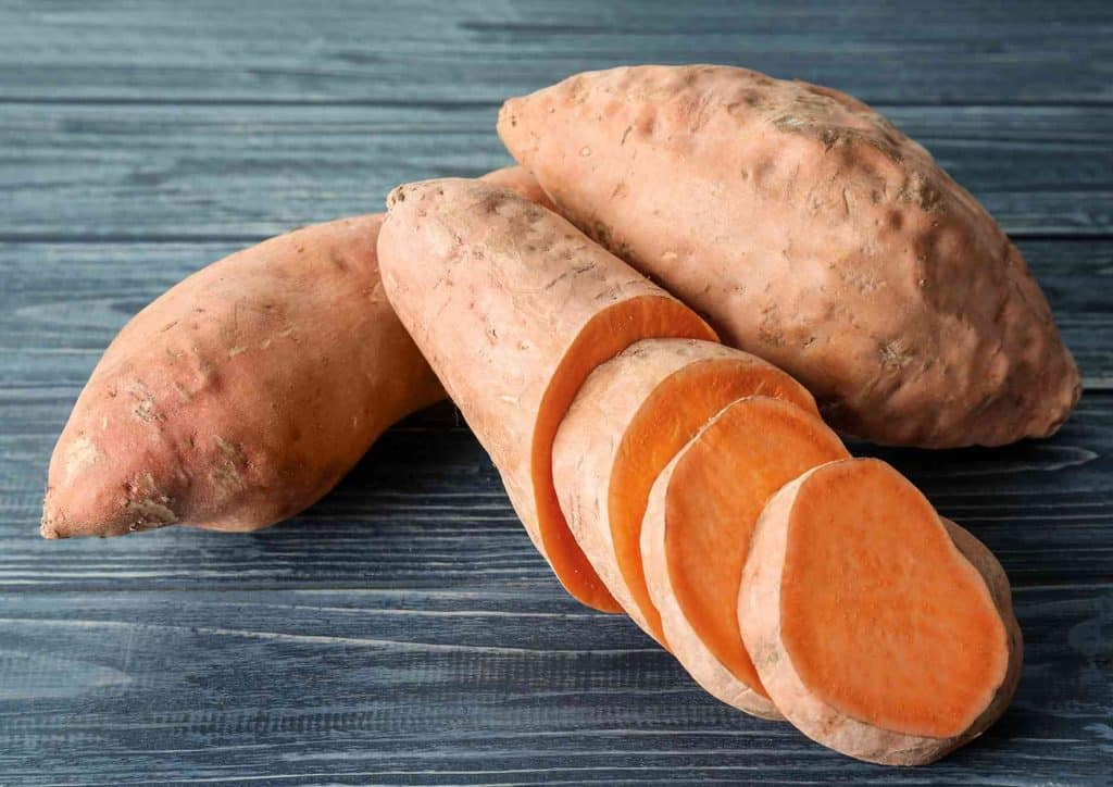 Is Sweet Potato Good for Weight Loss? 26 Sliced sweet potatoes stacked neatly on a rustic wooden table, showcasing their vibrant orange colour and texture.