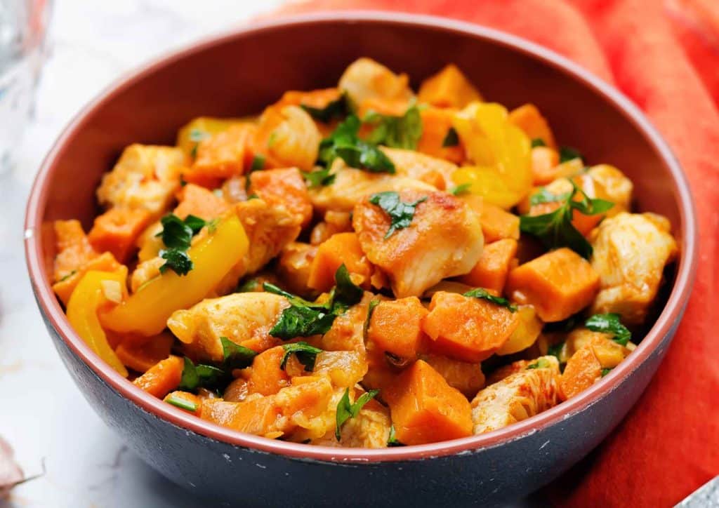 Is Sweet Potato Good for Weight Loss? 3 A bowl of chicken and sweet potato curry garnished with herbs, served with rice on a wooden table.