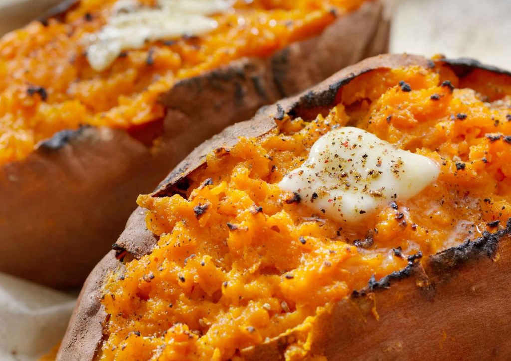 Is Sweet Potato Good for Weight Loss? 25 Two roasted sweet potatoes topped with melted butter and a sprinkle of spices on a wooden surface.