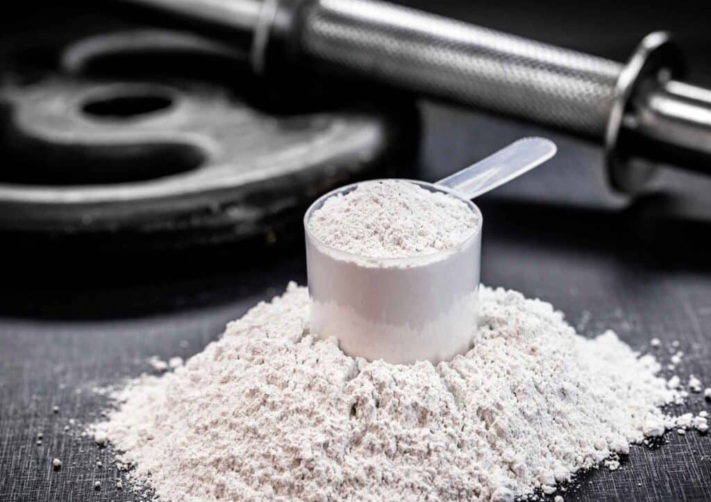 Is Creatine Good for Weight Loss? 1 A scoop of creatine powder placed beside a black dumbbell on a white surface.
