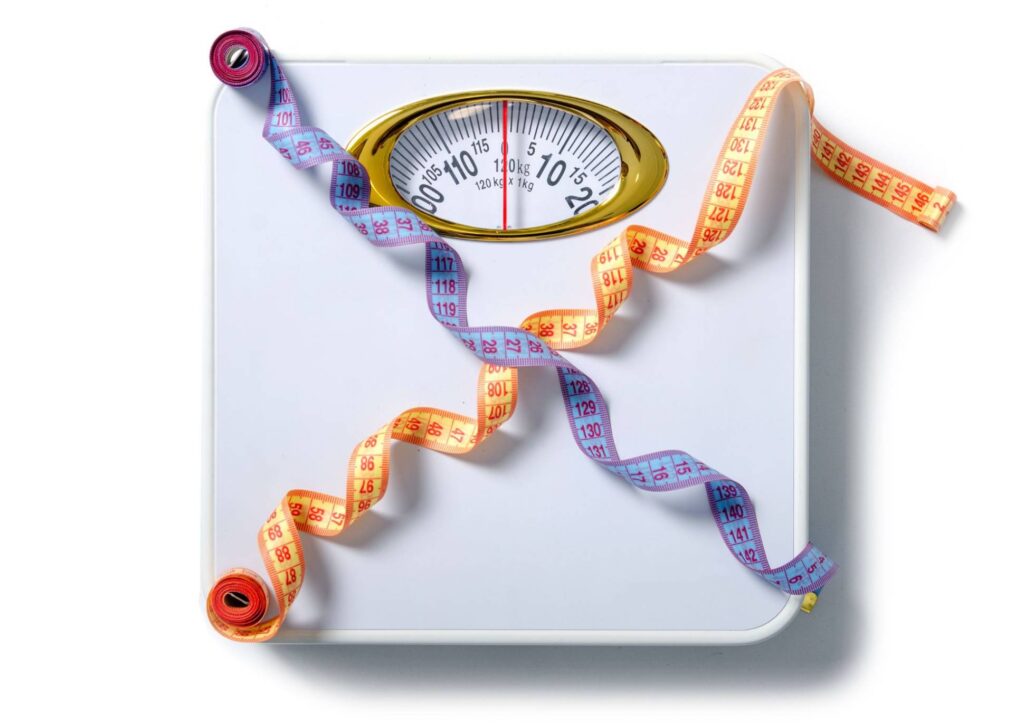 Is Creatine Good for Weight Loss? 5 A weight scale surrounded by a measuring tape and a decorative ribbon, symbolizing fitness and health tracking.