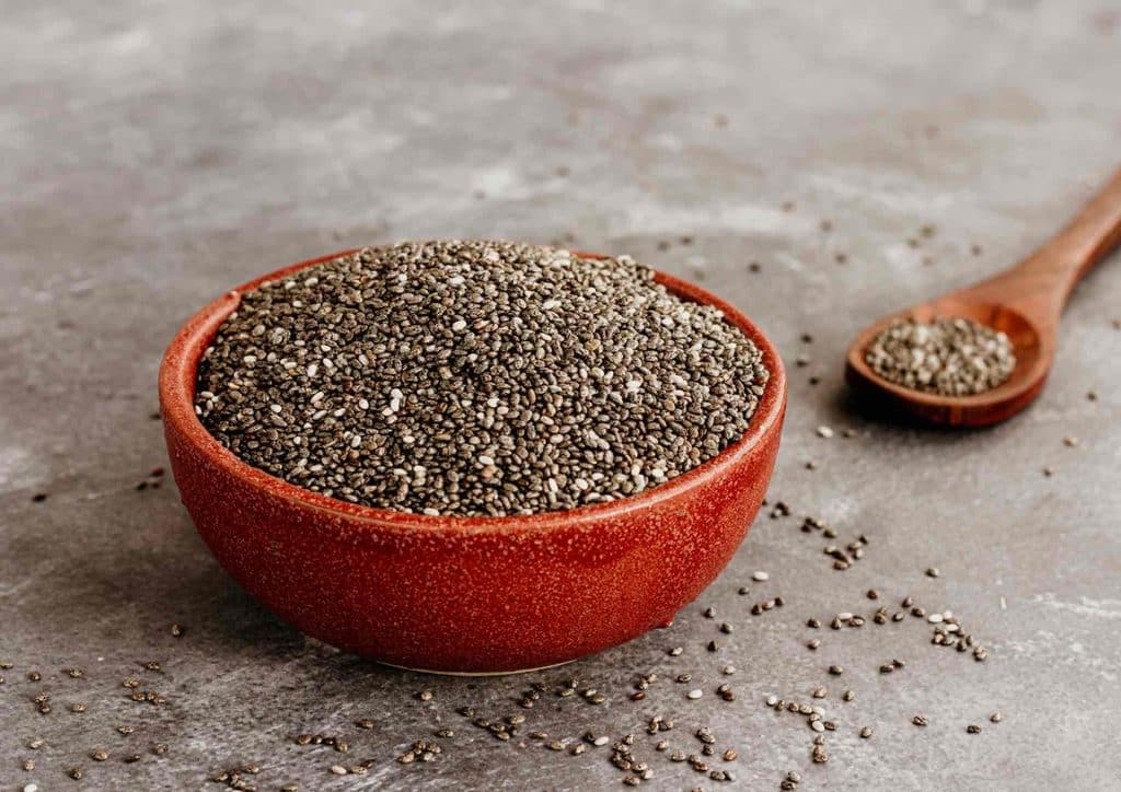 Do Chia Seeds Help With Weight Loss? 11 A bowl of chia seeds with a wooden spoon resting beside it, showcasing the seeds' small, round shape and texture.
