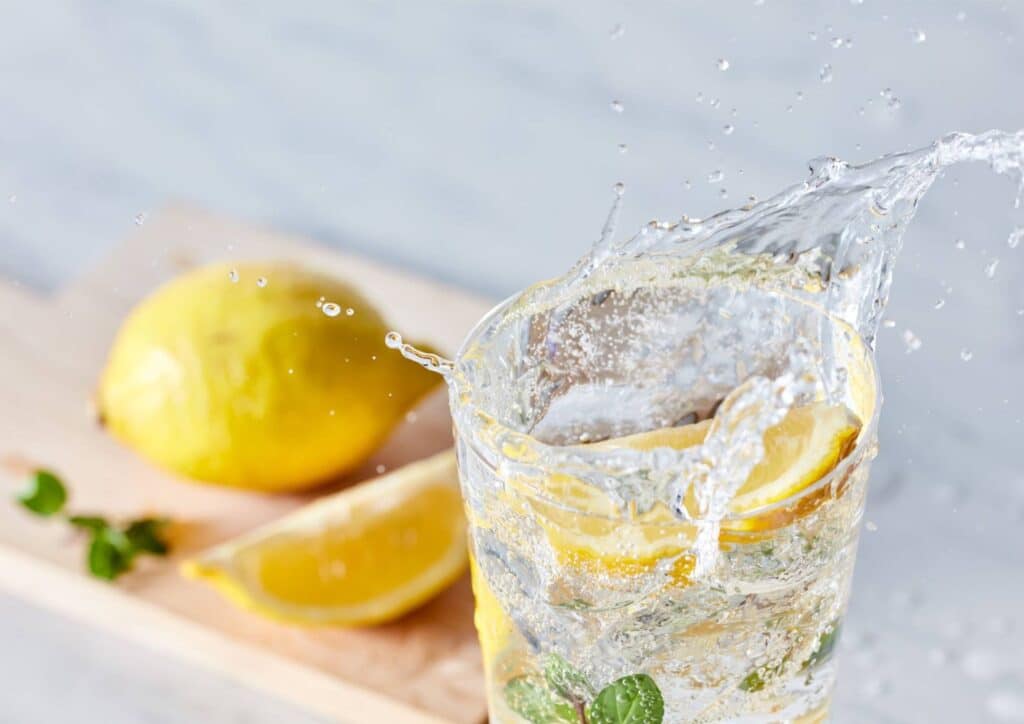 Does Lemon Water Help With Weight Loss? 3 A clear glass of water garnished with fresh lemon slices and mint leaves, placed on a wooden table.