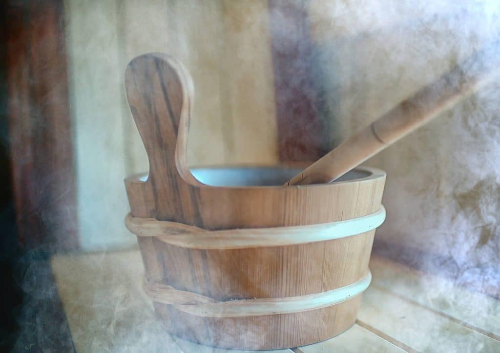 Do Saunas Help With Weight Loss? What Actually Happens 12 A wooden bucket with a wooden spoon resting on a rustic table surface.