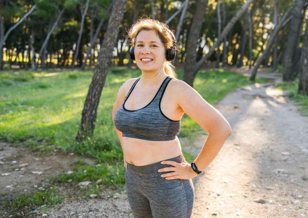 Do Saunas Help With Weight Loss? What Actually Happens 15 A woman in a sports bra stands confidently among trees in a wooded area, showcasing an active lifestyle.