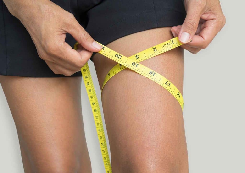 How to Tighten Skin After Weight Loss Naturally 9 A woman measuring her thigh with a tape measure, focusing on her fitness and body measurements.