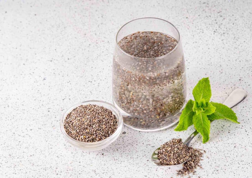 Do Chia Seeds Help With Weight Loss? 5 Chia seeds in a clear glass beside a silver spoon on a wooden surface.