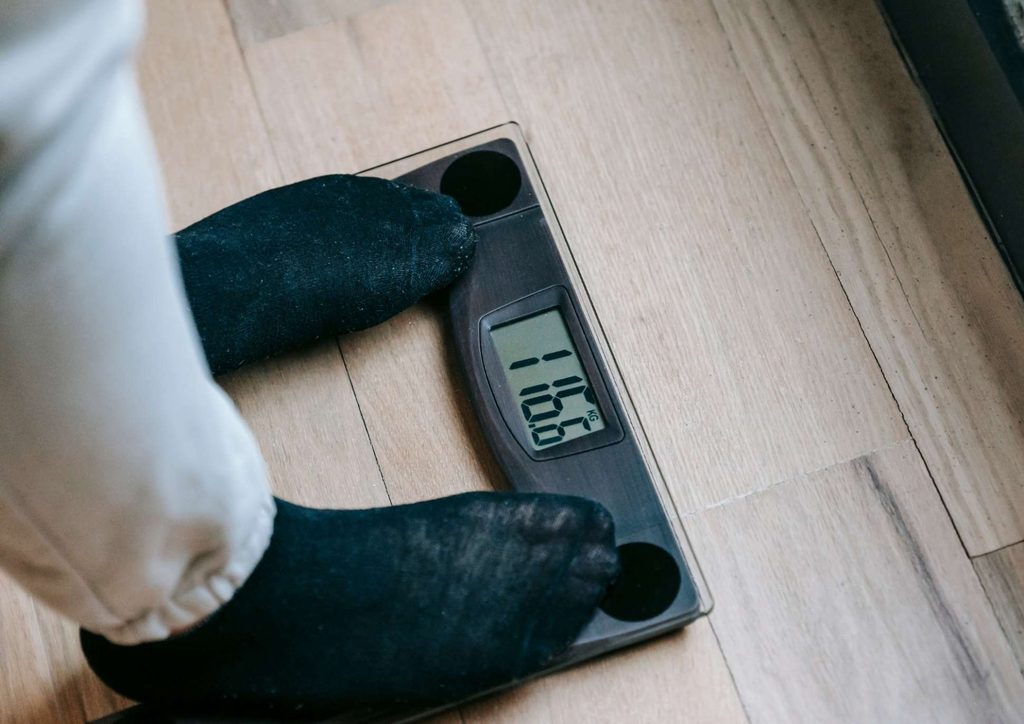 How to Break a Weight Loss Plateau, a Nutritionist's Approach 19 A person stands on a scale, feet firmly on the floor, measuring their weight.