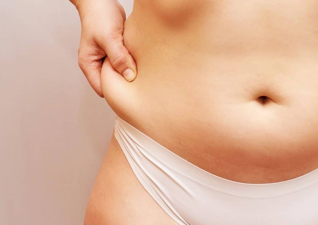 How to Tighten Skin After Weight Loss Naturally 14 A woman stands with her stomach exposed, showcasing her belly in a casual setting.