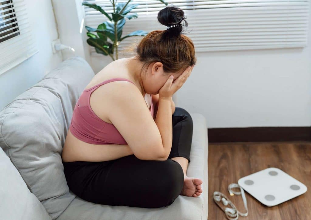 How to Break a Weight Loss Plateau, a Nutritionist's Approach 1 A woman sits on a couch, her head in her hands, conveying a sense of distress or deep contemplation.