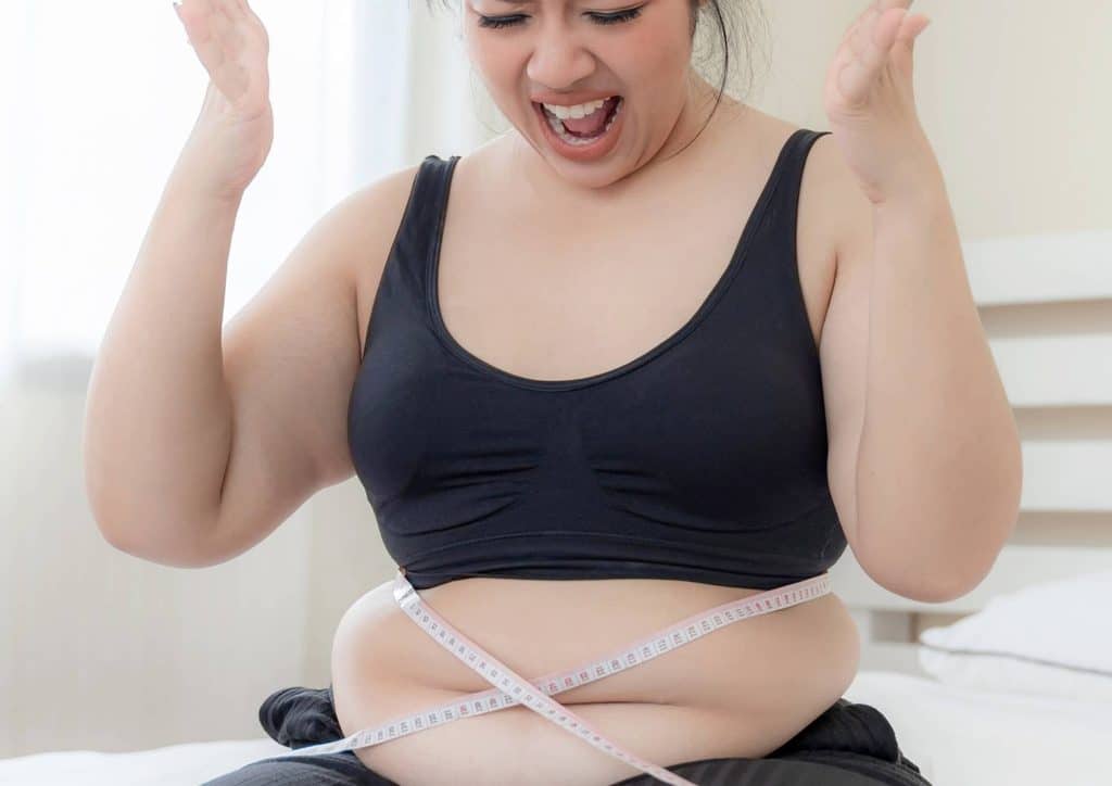 How to Break a Weight Loss Plateau, a Nutritionist's Approach 10 A woman measures her waist while holding her stomach, indicating concern or focus on her body measurements.