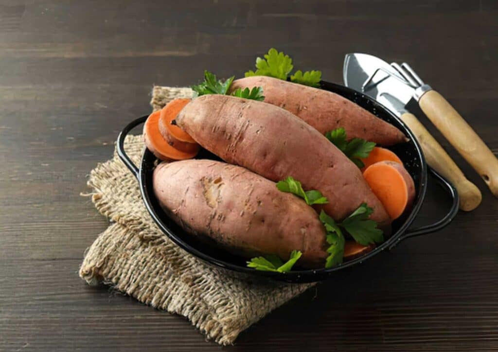 Is Sweet Potato Good for Weight Loss? 4 A black bowl filled with sweet potatoes, garnished with parsley and accompanied by sliced carrots.