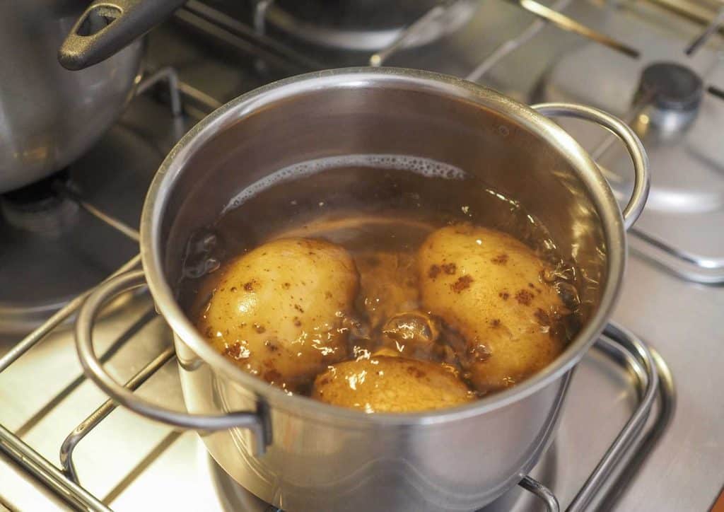 Is Sweet Potato Good for Weight Loss? 11 A pot on the stove containing boiling potatoes, with steam rising and a wooden spoon resting on the edge.